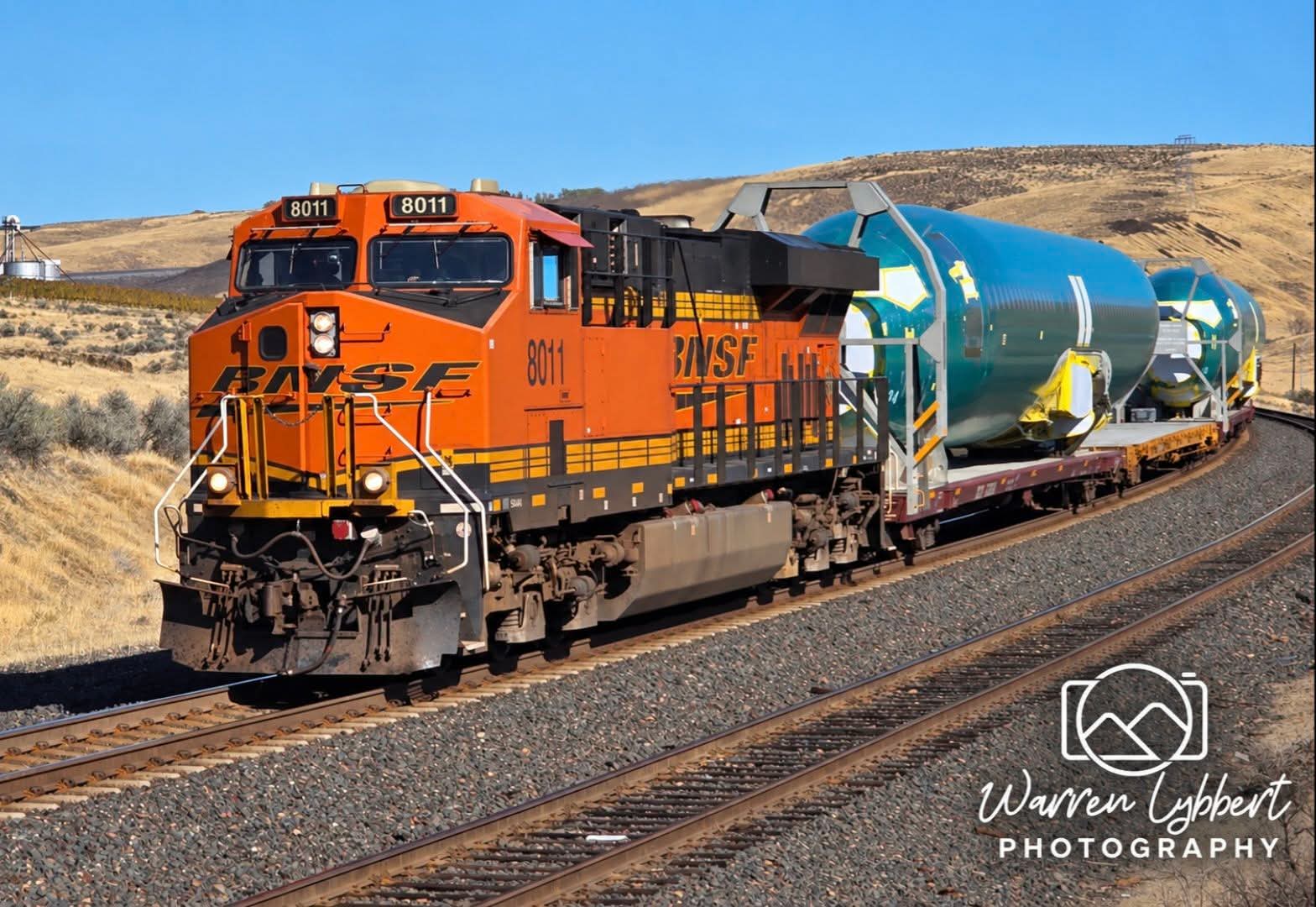 Orange BNSF locomotive 8011 hauling green airplane fuselages along curved track