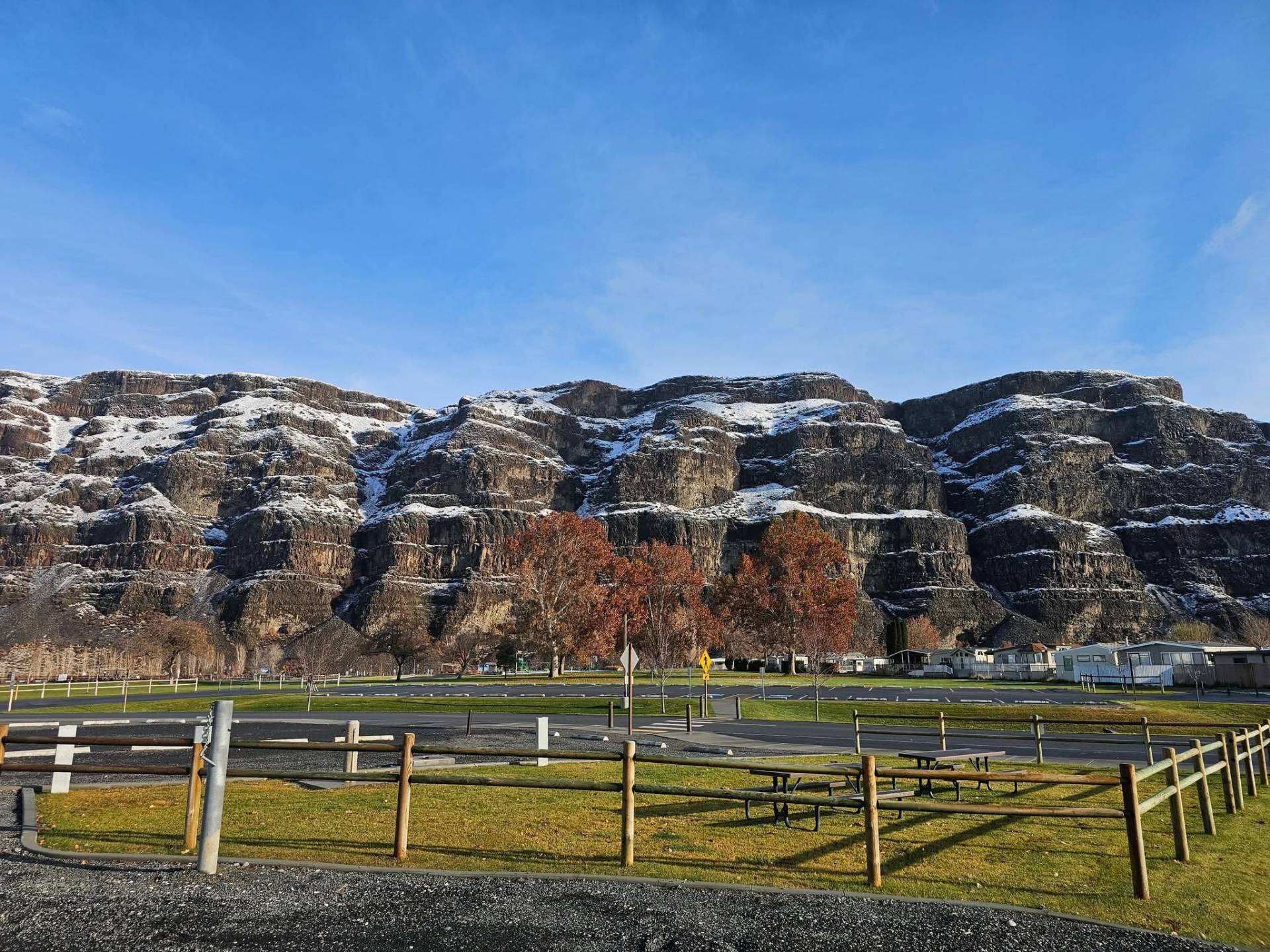 Snow-dusted basalt cliffs above autumn trees and a park