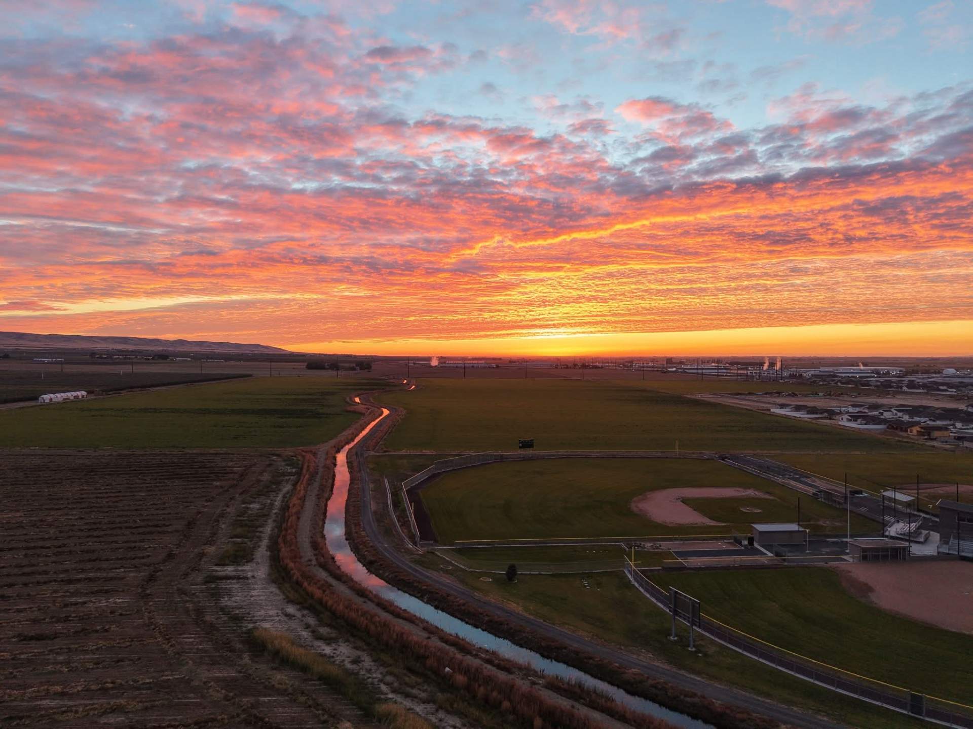 Aerial view of farmland, a winding canal and ballfields under a glowing sky